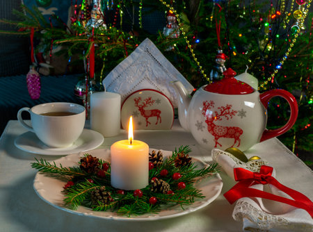 New Years tea party at the table with a teapot, candles on the background of the Christmas treeの写真素材