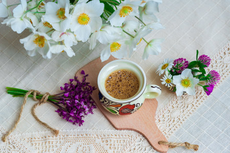 Coffee with foam and spring wildflowers on a white tablecloth.の写真素材