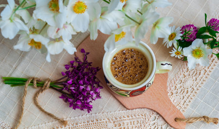 Coffee with foam and spring wildflowers on a white tablecloth.の写真素材
