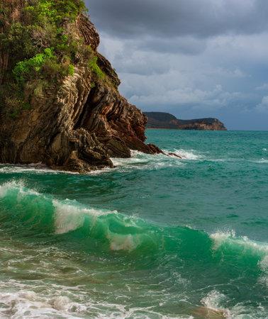 Azure vibrant breaking waves with white foam on rocky coast. Sunny beach with dramatic cloudy skyの写真素材