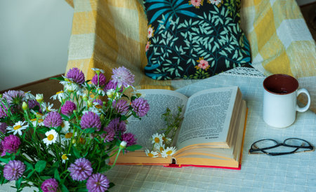 A bouquet of wild flowers, a cup of tea or coffee, a book with glasses on the table in the room.の写真素材