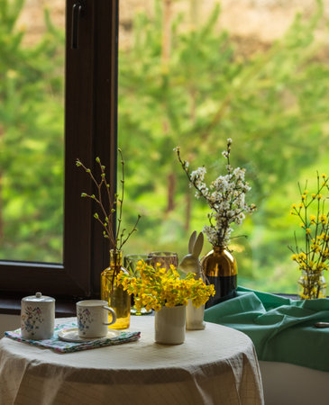 A cup of tea and spring flowers on a round table by the window overlooking the forest.の写真素材