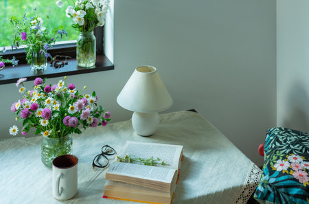 A bouquet of wild flowers, a cup of tea or coffee, a book with glasses on the table in the room.の写真素材