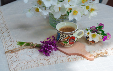 A cup of coffee and spring wildflowers on a white tablecloth. Sunlight and shadowsの写真素材