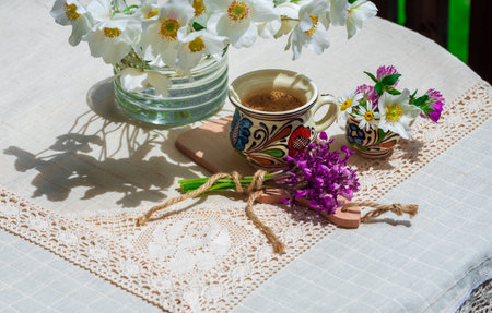 A cup of coffee and spring wildflowers on a white tablecloth.の写真素材