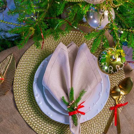 New Year's table setting in gold color, against the background of a decorated Christmas treeの写真素材
