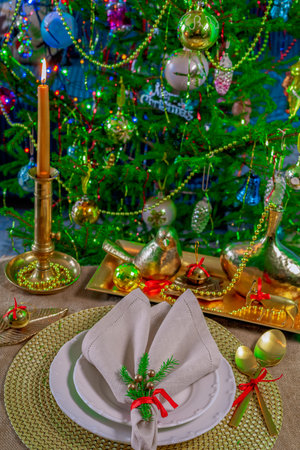 New Year's table setting in gold color, against the background of a decorated Christmas treeの写真素材