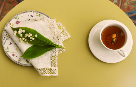 Lilies of the valley on a white napkin with lace and a cup of herbal tea