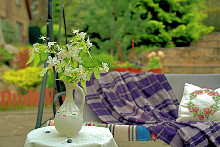 Apple blossoms on a table in front of a sofa swing in the courtyard of a country house.の写真素材