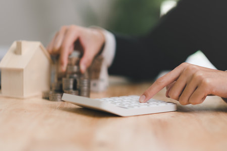 Real estate agent calculates numbers on financial documents with calculator, interest rate...