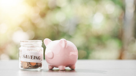 siveing text in a piece of paper and coins in a glass jar, pink piggy bank, all on the table, savings concept, financial growth, retirement preparation Managing future funds, creating spending habitsの写真素材