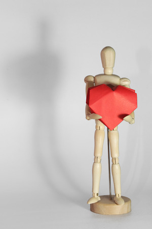 wooden manikin holding heart, isolatedの写真素材