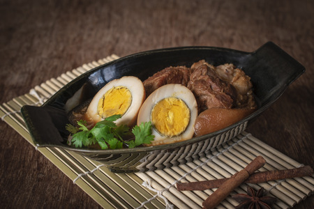 stewed eggs and pork in black bowl and spices place in front of on wood sieve and wood backgroundの写真素材