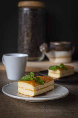 layer vanilla flavoured cake place on white plate on the wooden table there are white cup and black plate and coffee bean in glass bottles and watering ceramic place backside.の写真素材