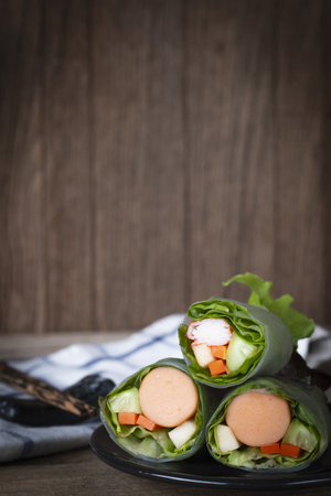 Salad rolls on black plate placed on a wooden table with chopsticks and White Blue Striped Fabric placed backside.の写真素材