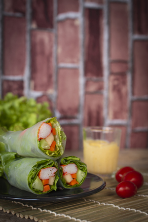 Salad rolls on black plate placed on a wood sieve there is tomatos placed beside and salad dressing placed backside.の写真素材