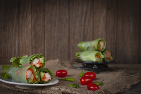 Salad rolls on white plate placed on a sack there is tomato and chilli placed beside and Salad rolls...