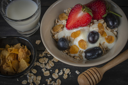 Yoghurt mix oatmeal, strawberry and grape topping in white bowl on the wood table with oatmeal, cornflakes and milk in glass placed aroundの写真素材