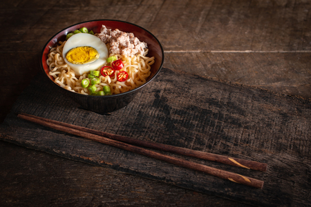 Instant noodle with pork, egg and vegetables on black bowl on the wood table there is chopstick placed in front of.の写真素材