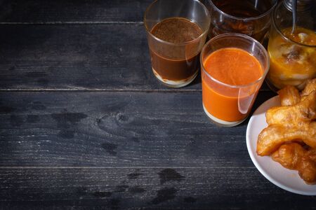 Traditional Thai hot tea with milk on the wood table there are Traditional Thai hot coffee, deep-fried doughstick (patongko), hot tea, Kettle and soft-boiled egg plated around.の写真素材