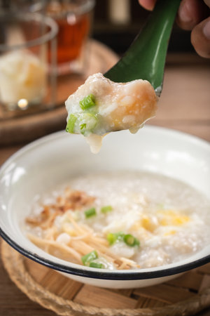Close-up of a person serving rice porridge or pork congee for breakfast, boiled eggs, fried dough,...