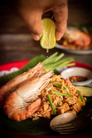 Close-up of a person squeezing lime juice on stir-fried noodles, Pad Thai, Thai foodの写真素材