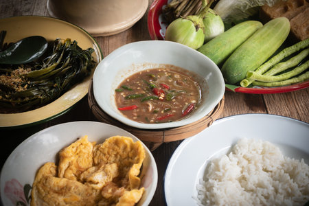 Shrimp paste chili dip, steamed rice, stir-fried morning glory with chili paste and omelet are placed on the dining table. Retro Thai style image.の写真素材