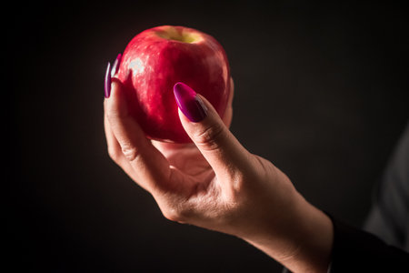 Image of a person holding an apple in their hand, black background.の写真素材