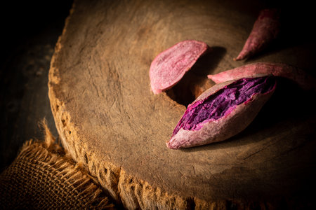 Steamed, cooked and raw purple sweet potatoes on a wooden cutting board.