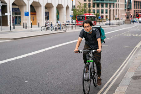 LONDON, ENGLAND - JULY 24, 2020:  Young asian male Deliveroo courier cyclist on a lunchtime food delivery during the COVID-19 coronavirus pandemic - 128のeditorial素材