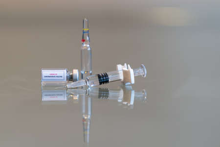 A sideways mini vial of COVID-19 Coronvavirus vaccine with a syringe on the right and an ampule in the rear - 131の写真素材