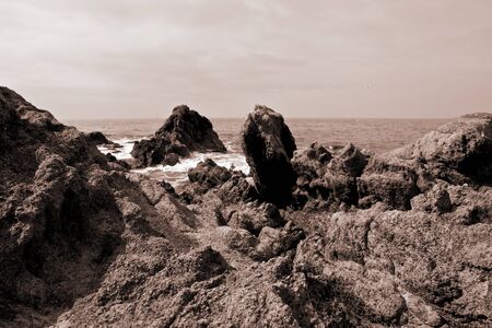 Black and white image of a view on the Mediterranean Sea with harsh volcanic rocks in the foreground