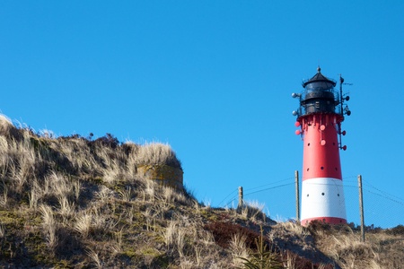 Small lighthouse against a clear blue sky with a dune full of beach grassの写真素材