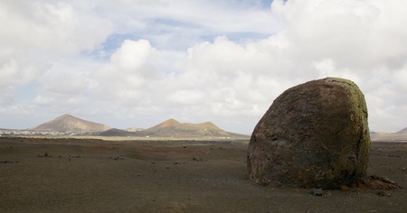 Wide angle shot of the barren volcanic landscape of Lanzarote island with a lava bomb in the foregroundの写真素材