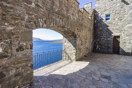Opening in an ancient stone wall letting in the bright sunlight from the Scottish loch outsideのeditorial素材