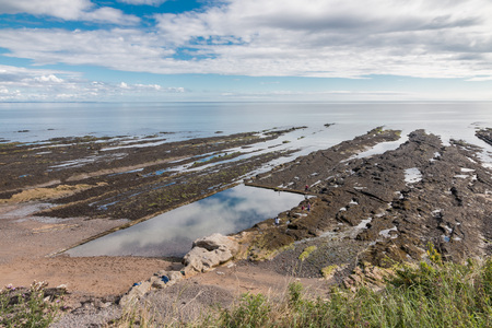 Rocky shore with tidal pools and reflections of the summer sky at the coast of St. Andrews, Scotlandの写真素材