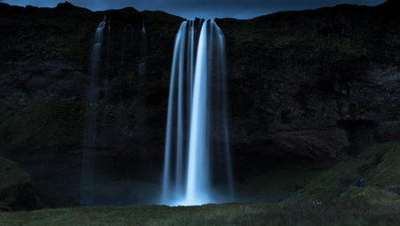 Night shot of world famous Seljalandsfoss, a majestic waterfall in southern Iceland, coming down over a cliff, fed by a glacierの写真素材