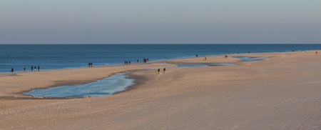 Beach scene on Sylt island, Germany, with hikers walking along the shoreline and beach grass on a dune in the foregroundの写真素材