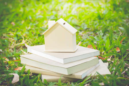 Model of house place on pile of notebooks on green grass background.a model of house with book .の写真素材