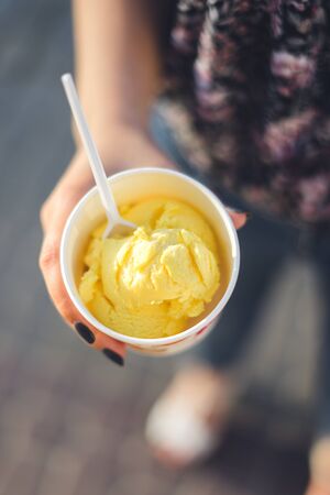 A woman's hand holds fruit ice cream. Mango ice cream in a cup.の写真素材