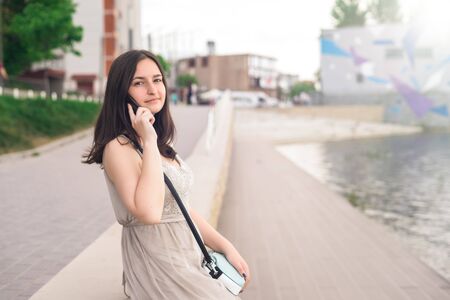Girl in gray dress with telephone. Girl on the waterfront of the lake in summer dayの写真素材
