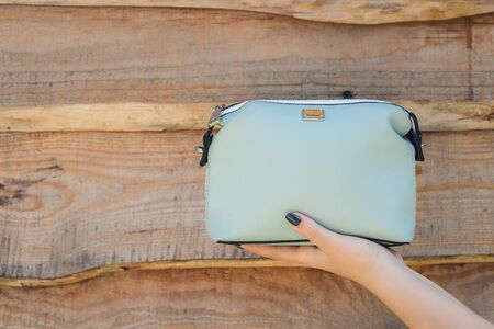 Woman hand holds handbag on wooden background. Blue little bagの写真素材