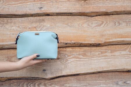Woman hand holds handbag on wooden background. Blue little bagの写真素材