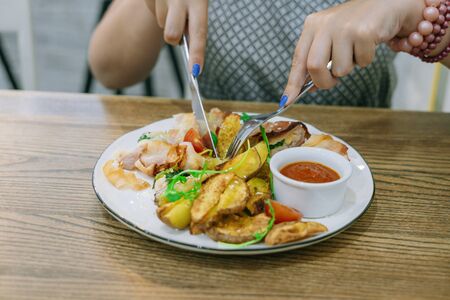 Female hands with knife and fork cut meat with potatoes. Female hands with manicure. Restaurant dishの写真素材