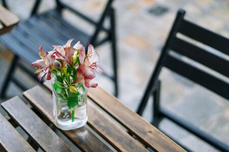 Beautiful alstroemeria in vase on wooden table in summer cafe. Gentle summer bouquet in a glass vase. Pink flowers on a sunny day.の写真素材