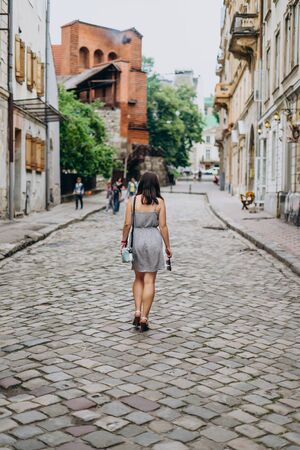 Young woman walking in the sunny city streets. Brunette woman in sundress and sandals. Old town...