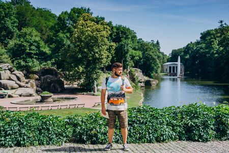 Sofia Park, Ukraine. Handsome man with a beard in a dendrological park. Man with a backpack on the background of the lake with a fountain and a white gazebo.の写真素材