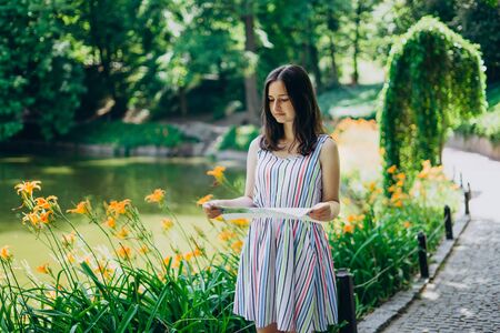 Sofia Park, Uman. Beautiful girl with a tourist map walks in the summer park. The girl in a dress walks by the lake. Excursion to a beautiful park with a lake, flowers and tall treesの写真素材
