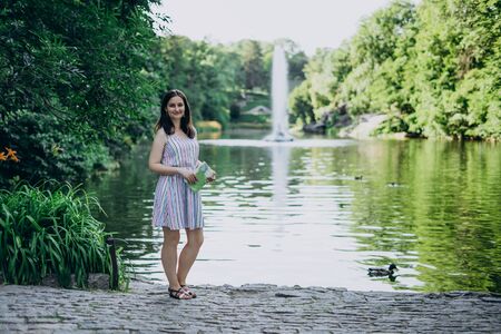 Uman, Ukraine. Smiling girl on a background of high fountain and lake. Girl in a summer dress on a background of a beautiful tall fountain. Lake in the park and splashing fountainの写真素材