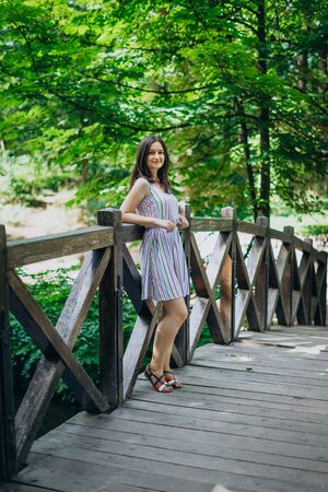 Sofia Park, Uman. Smiling girl in a summer board on a wooden bridge. The girl stands on the bridge among the green summer park. Walk in the summer green forestの写真素材